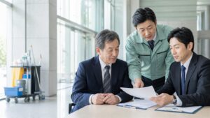 清掃用具のある建物内で3人が書類を確認する相談イメージ